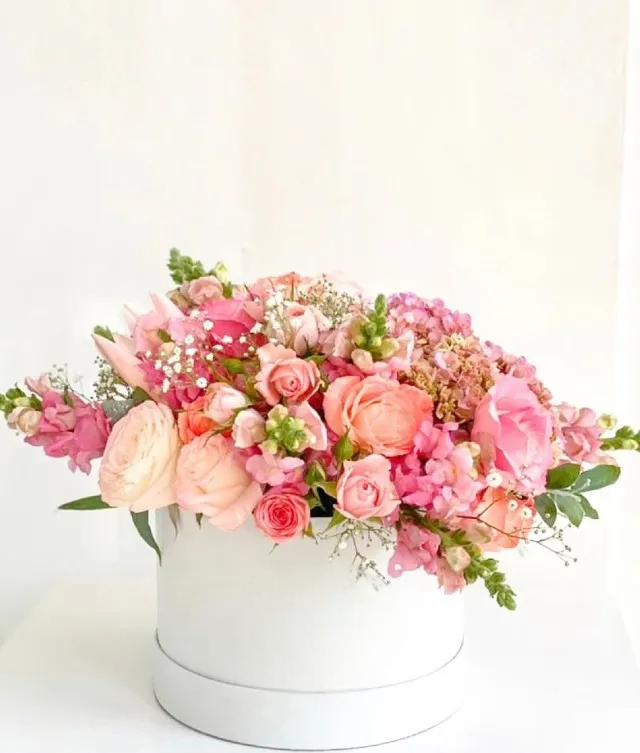 beautiful flower arrangement, including various shades of pink roses, pink hydrangeas, pink snapdragons in a white round box
