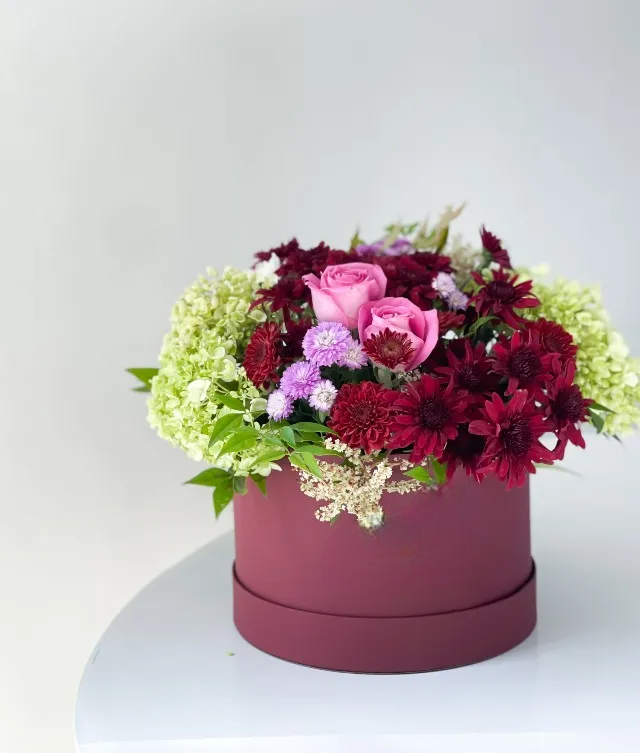 A red chrysanthemum and green hydrangea flower arrangement in a maroon-colored box