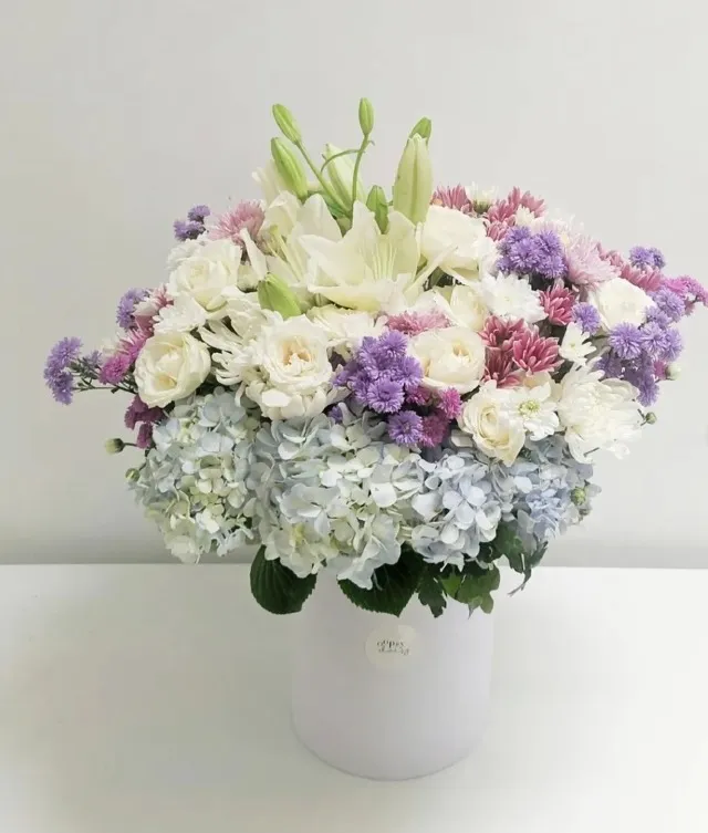 a beautiful arrangement with roses, hydrangeas, chrysanthemums, and lilies in a white box.