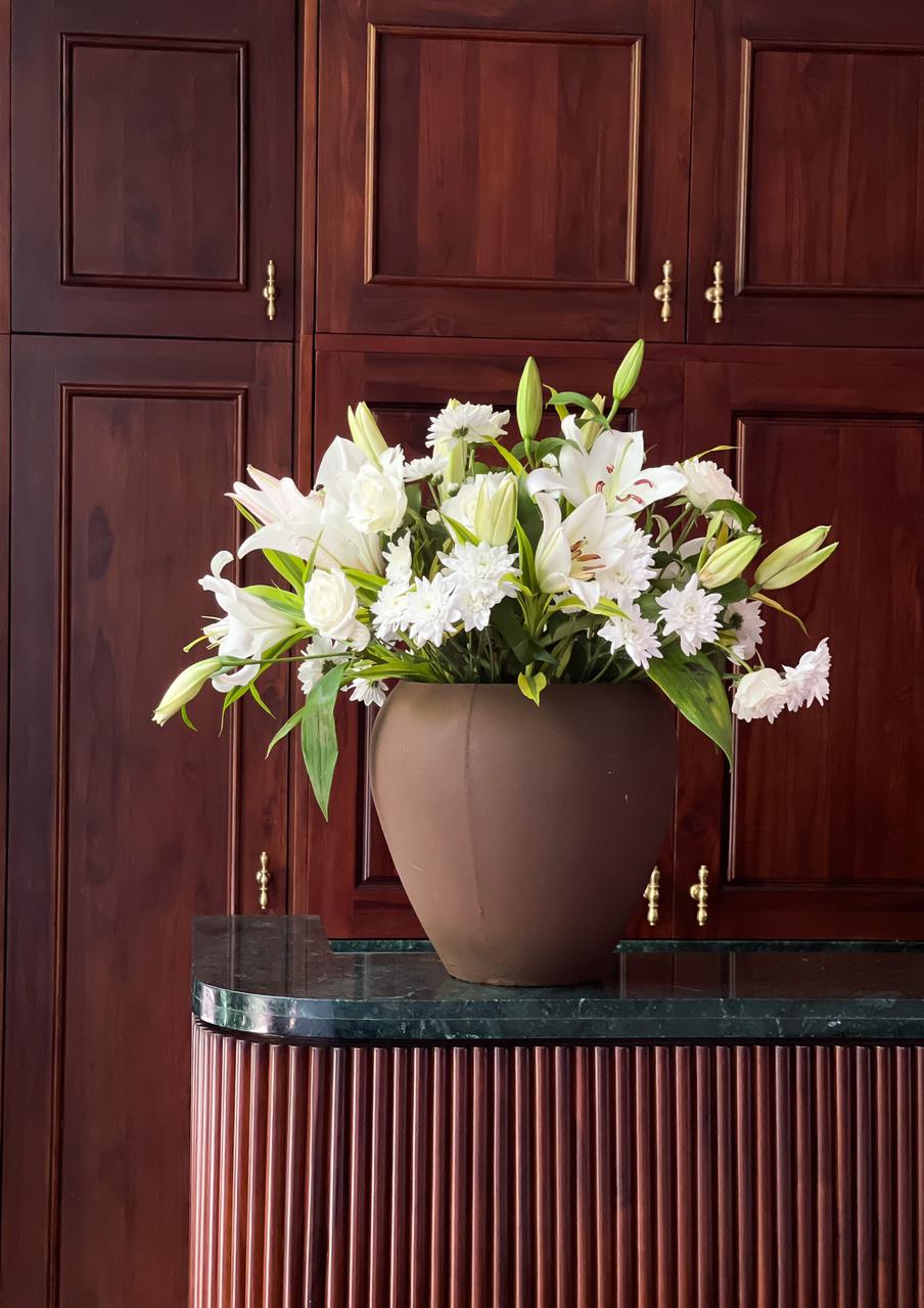 Surprise your loved one with an exquisite flower arrangement featuring pristine white roses, elegant white chrysanthemums, and delicate white lilies, all beautifully presented in a classic brown pot. A timeless gift that radiates pure elegance and charm