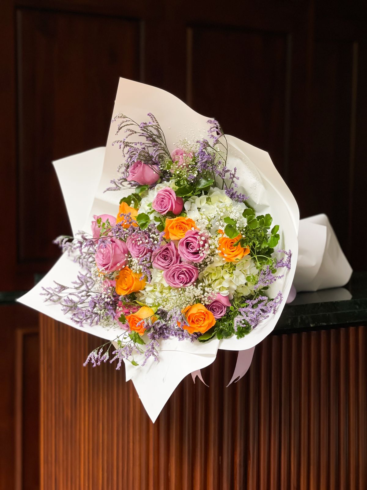 Surprise your loved ones with a stunning bouquet featuring vibrant purple and orange roses, complemented by lush hydrangeas, all beautifully arranged and elegantly wrapped in luxurious ivory. A captivating display of color and elegance, this bouquet is sure to brighten their day and leave a lasting impression