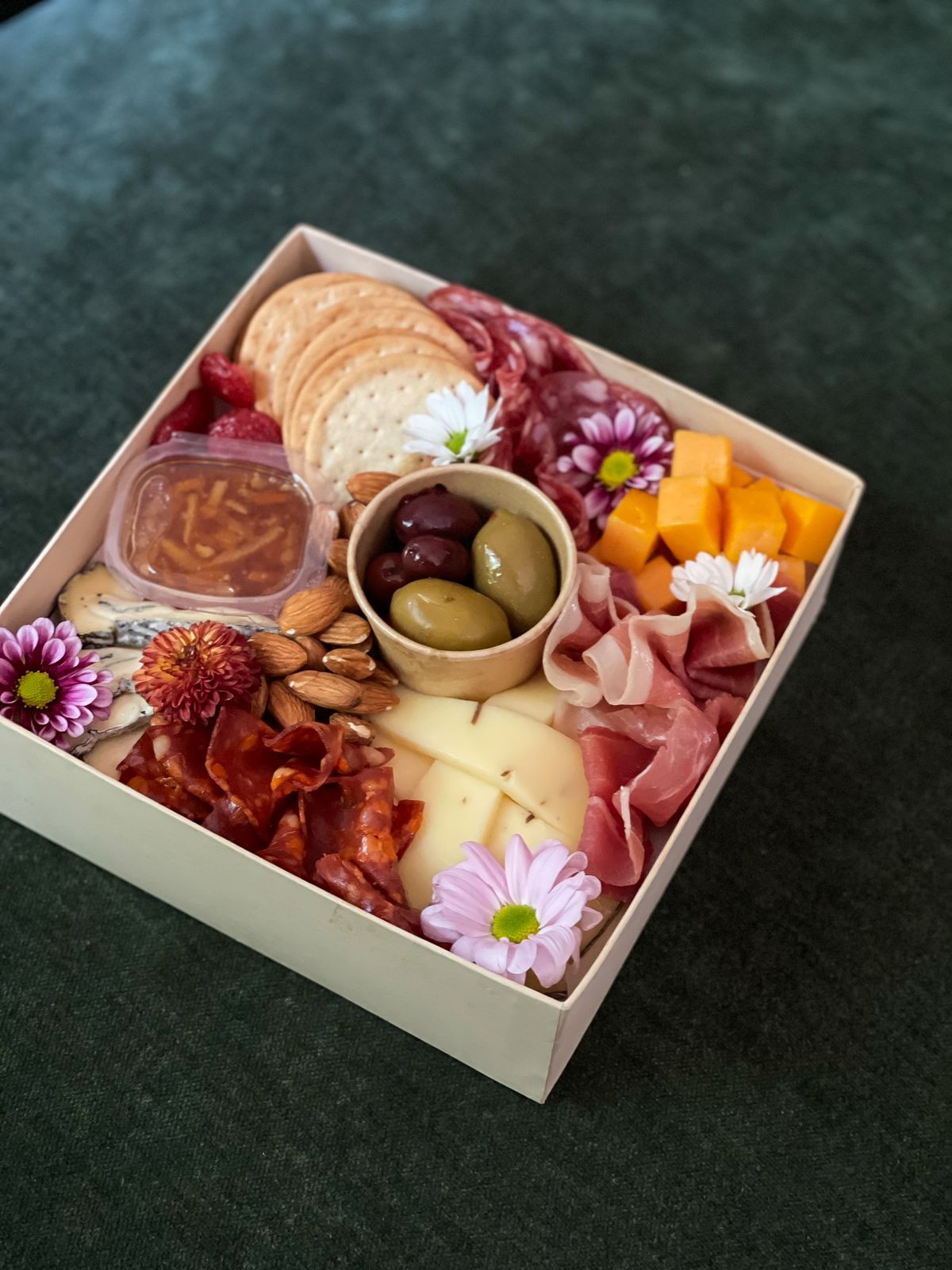 Treat someone special with a delightful petite platter for two, featuring a selection of exquisite cheeses and premium cold cuts. This beautiful platter includes: - Ashen Blue Cheese, Red Cheddar Cheese, Truffle Gouda, Prosciutto Parma, Salame Milano, Spianata Piccante, Almonds, Marmalade, Dried Strawberries, Olives, Crackers with Fresh Flowers. Perfect for a thoughtful and delicious gift!