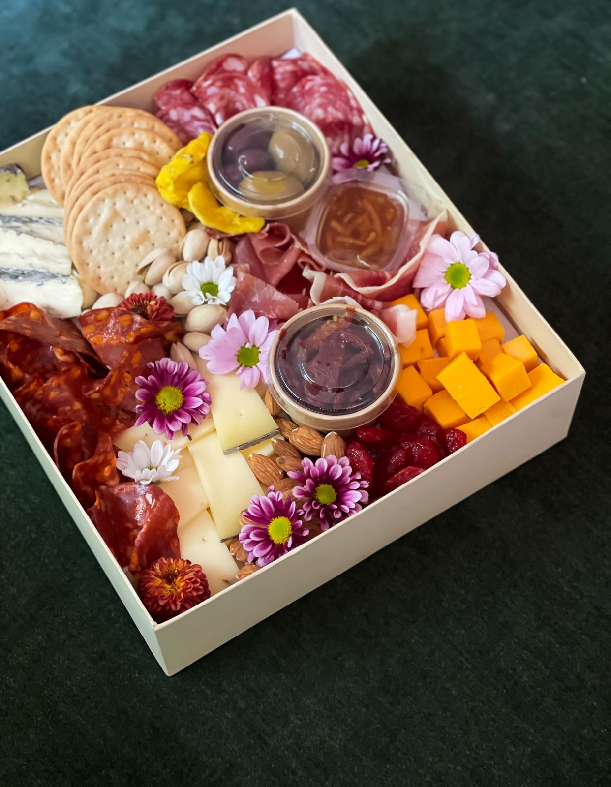 Treat someone special with a delightful petite platter that serves 5 to 6 people, featuring a selection of exquisite cheeses and premium cold cuts. This beautiful platter includes: - Ashen Blue Cheese, Red Cheddar Cheese, Truffle Gouda, Prosciutto Parma, Salame Milano, Spianata Piccante, Almonds, Marmalade, Dried Strawberries, Olives, Crackers with Fresh Flowers. Perfect for a thoughtful and delicious gift!