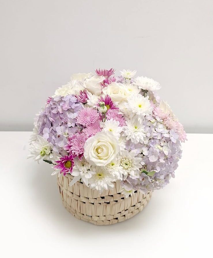 This charming cane basket is filled with the delicate beauty of roses, soft chrysanthemums, and lush hydrangeas.